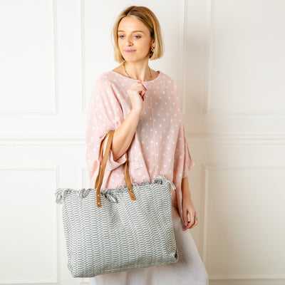 The grey Woven Beach Bag made from woven cotton with a contrasting brown faux leather strap 