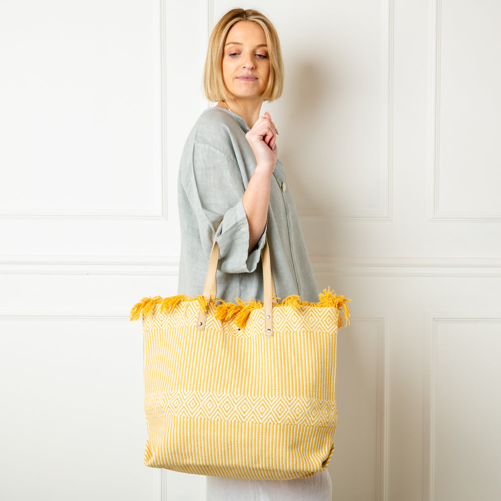 The yellow Woven Beach Bag made from woven cotton with a contrasting brown faux leather strap 
